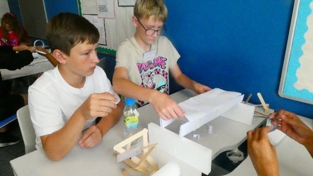 Two students building a paper bridge between two stands about 60 cm apart