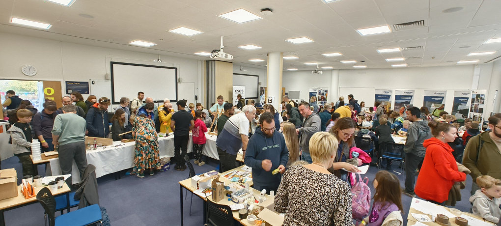 A room full of people visiting the CSES hands-on activities, talking to volunteers