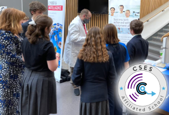 Students and teachers stand around a live science demo at a school, with the 'CSES Affiliated School' badge overlaid on the corner of the image