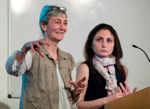 A female academic giving a talk and sharing a joke with someone in the audience, while another academic looks on