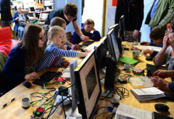 A mother with her young children at a coding workshop, assisted by a volunteer