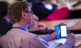 A conference delegate making notes and reading from their mobile device